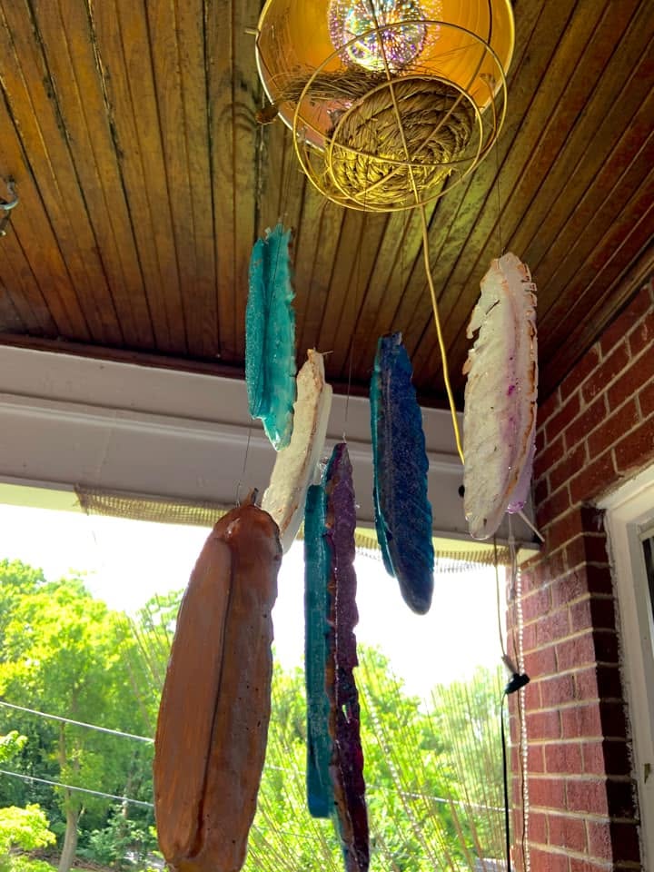 Colorful resin feathers hanging beneath a gold-painted lamp on a porch